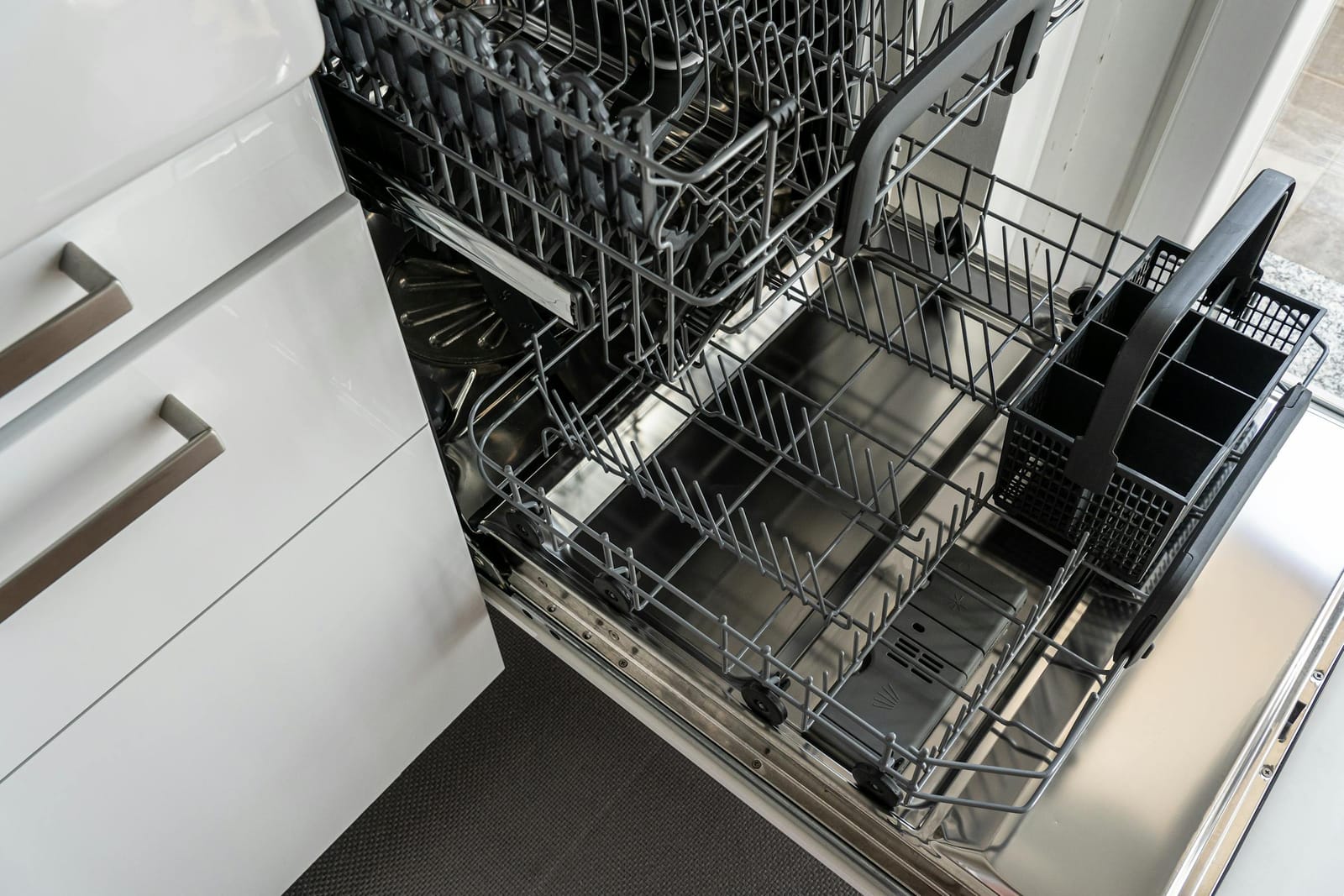 Built-in stainless steel dishwasher with door open showing empty racks in a modern white kitchen