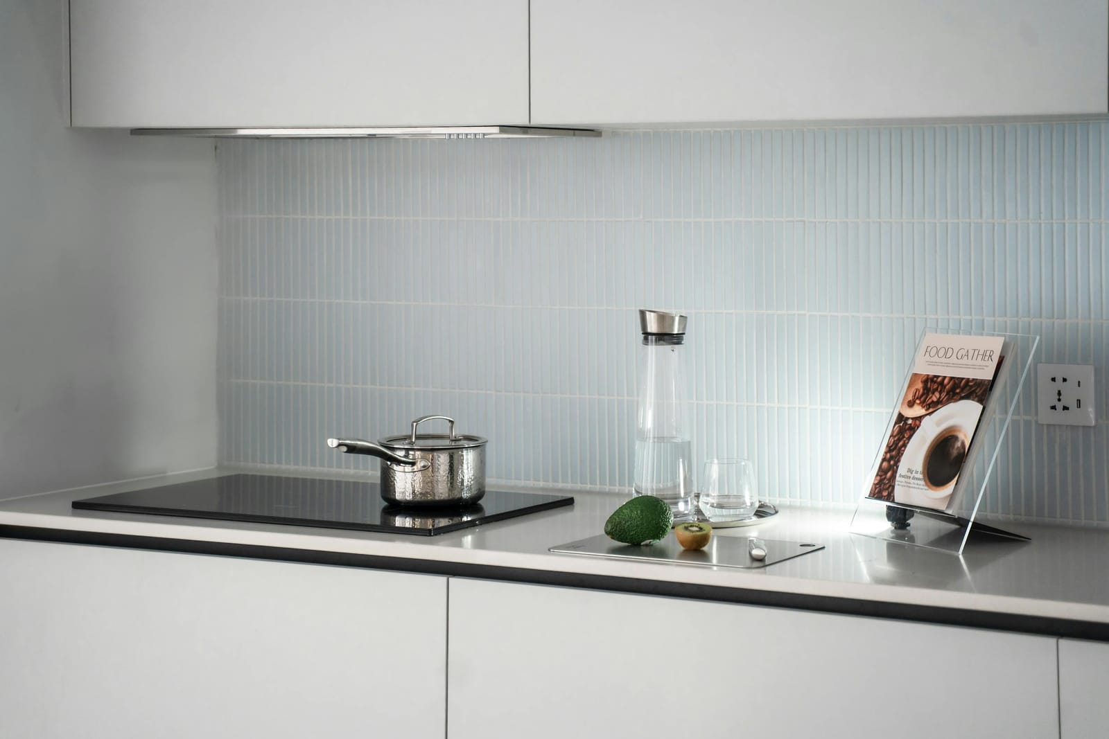 Black induction cooktop with a single pot, set in a minimal white kitchen with a slim range hood