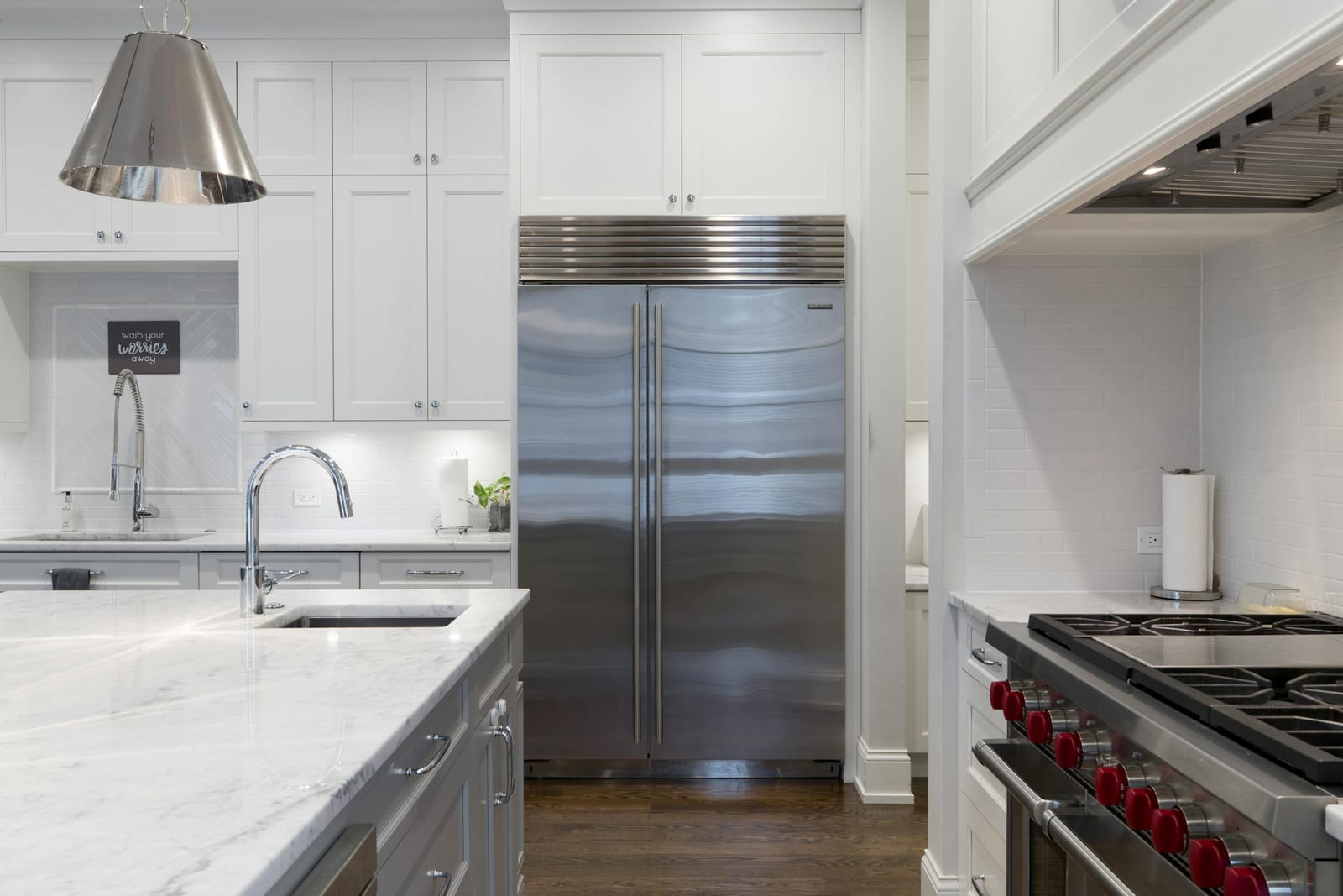 Stainless steel built-in refrigerator in a modern white kitchen with marble island