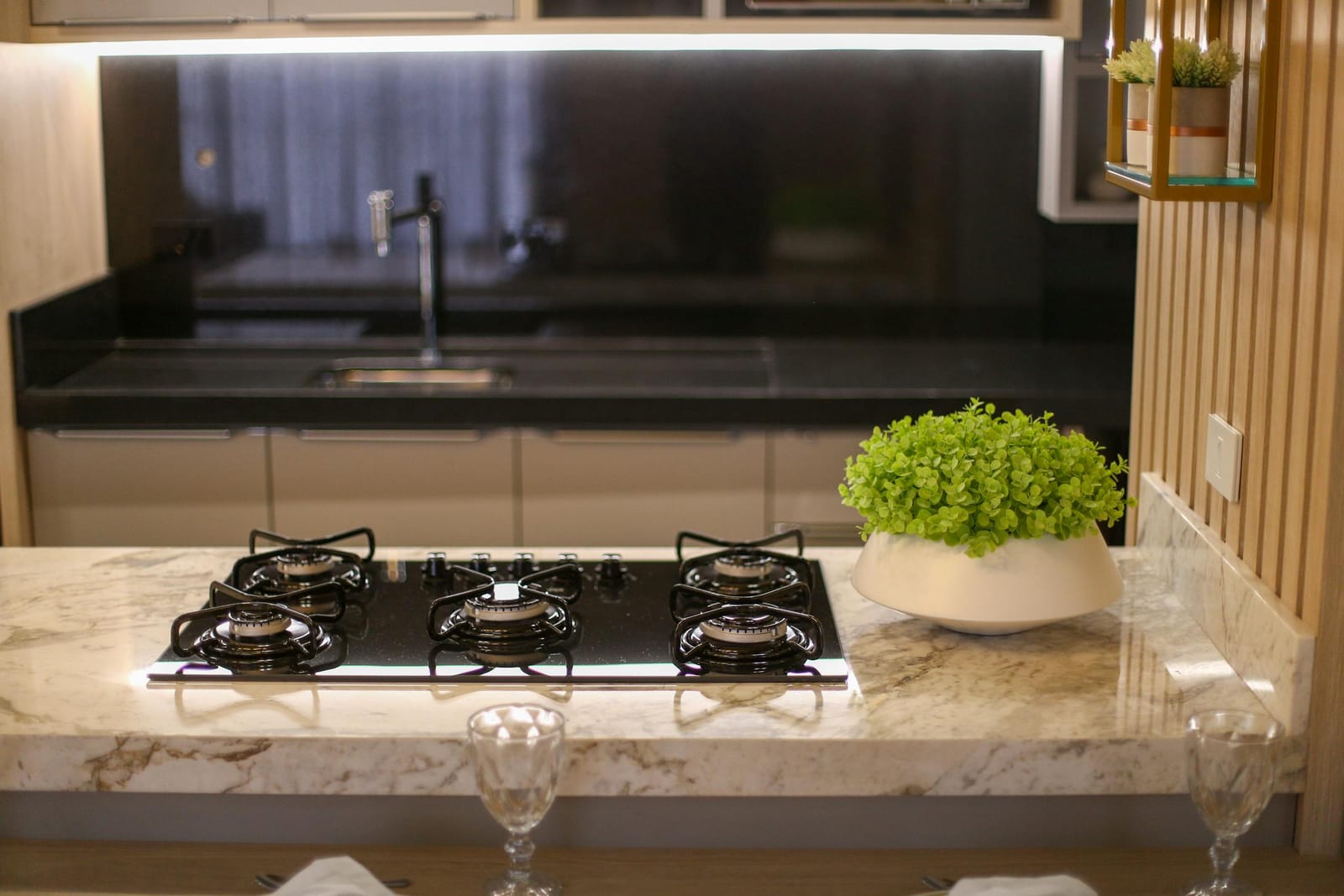Black five-burner gas cooktop set into a white marble kitchen bench with indoor plants in the background