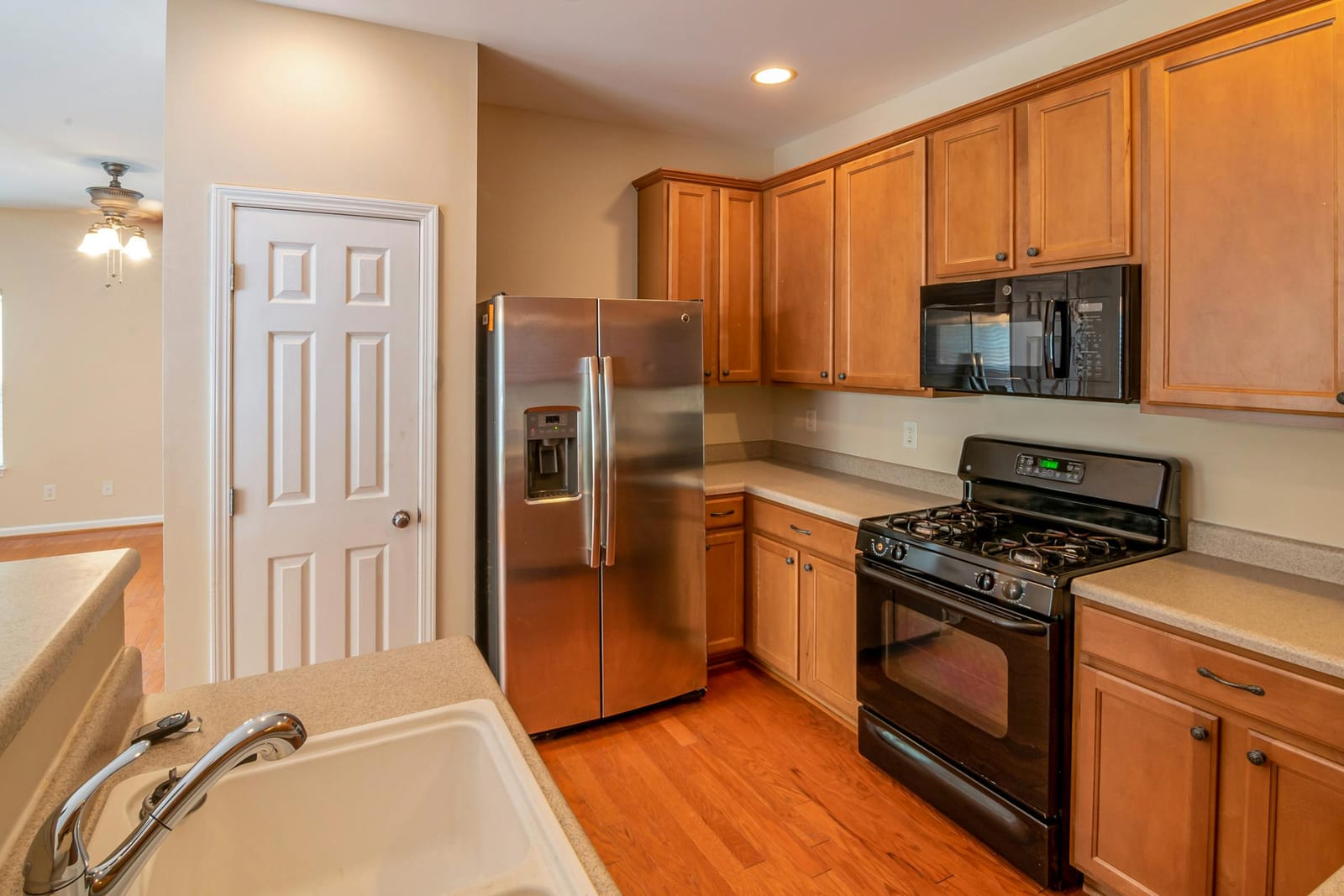 Freestanding black gas range with oven below and gas burners on top, set in a kitchen with wooden cabinets and a stainless side-by-side fridge