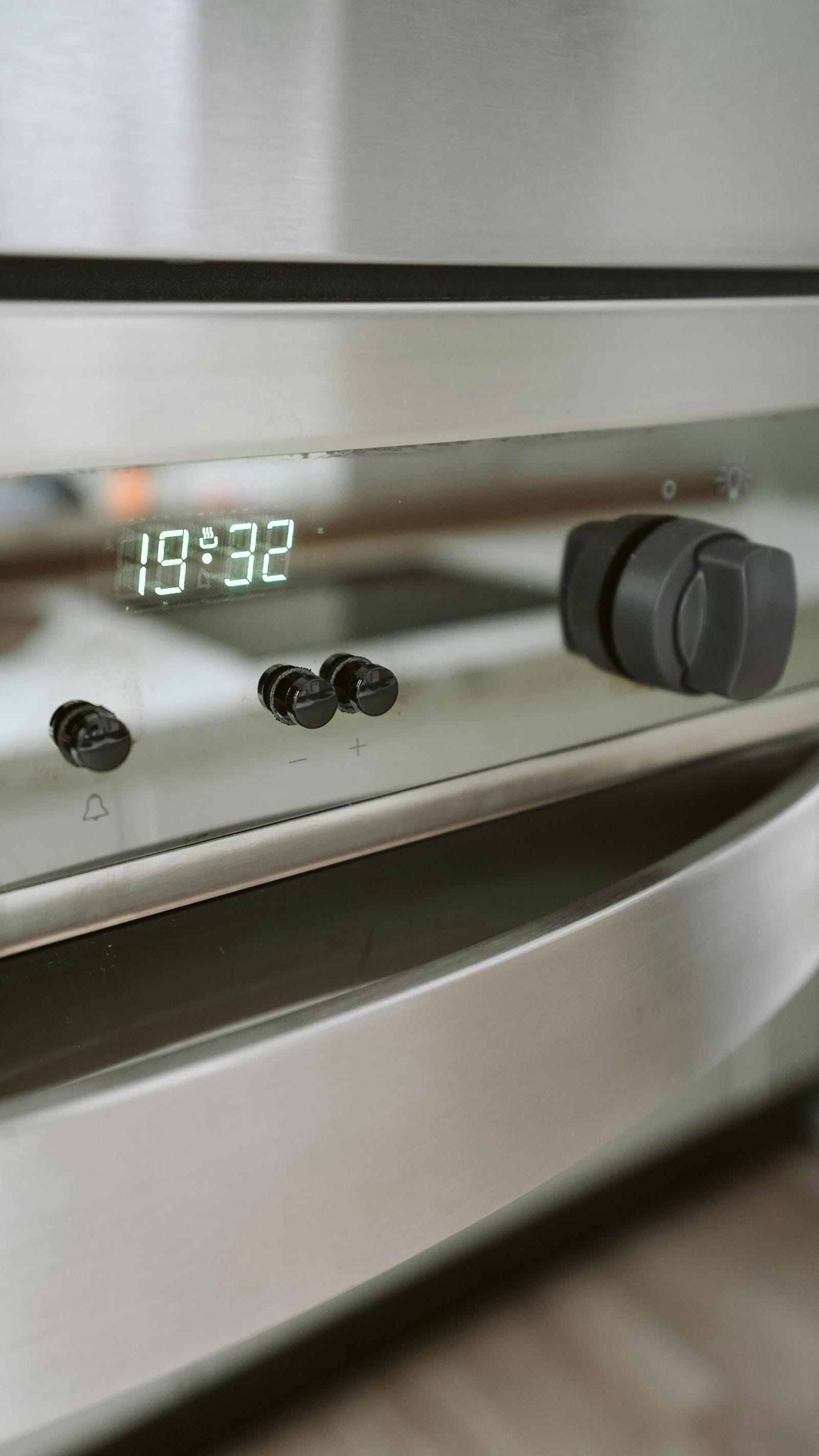 Close-up of a modern stainless-steel oven control panel with digital display and knobs
