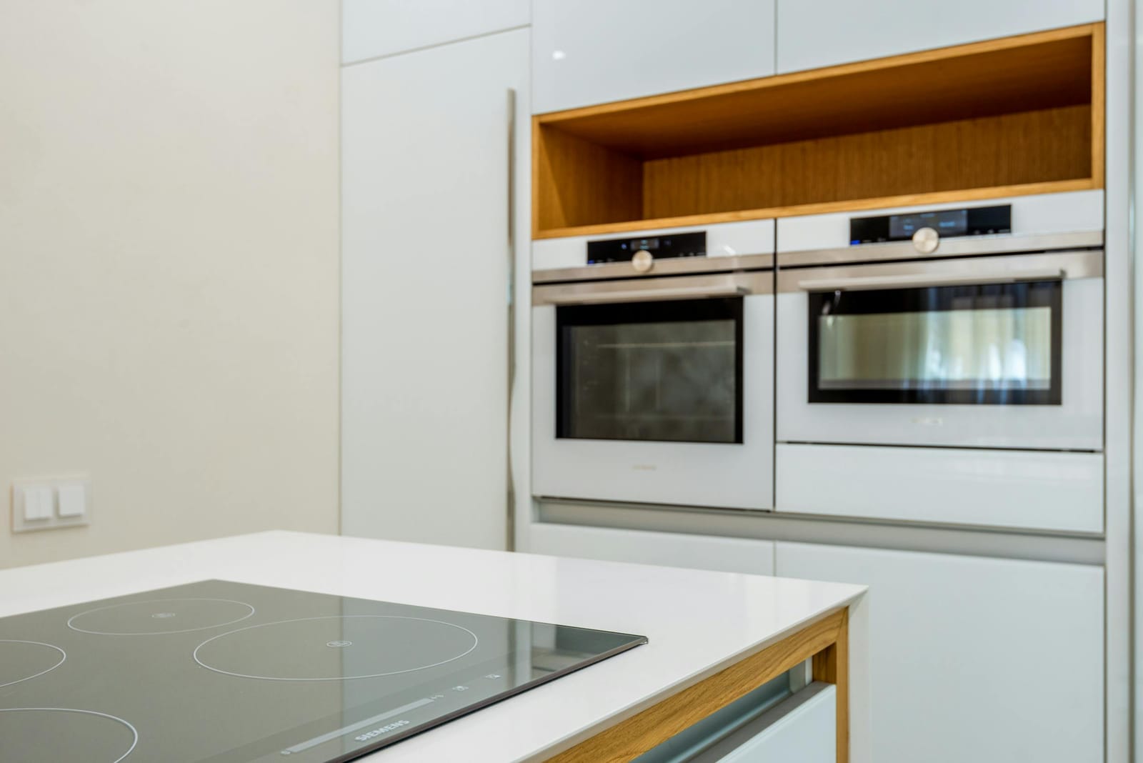 Pair of built-in wall ovens stacked in a modern white kitchen with an induction cooktop on the bench